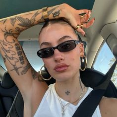 a woman with tattoos on her arm sitting in the back seat of a car wearing sunglasses