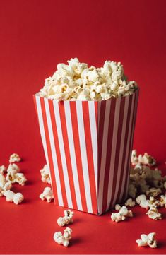 a red and white striped paper bag filled with popcorn on top of a red surface