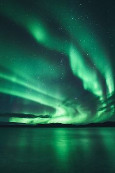 the aurora bore is glowing green in the night sky over water with stars above it