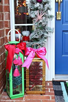 a green lantern with pink ribbon and christmas decorations in front of a blue door decorated for the holidays