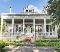 a white house with pillars and columns on the front porch is surrounded by greenery