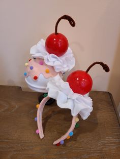 a cake with two cherries on top of it sitting on a wooden table next to a wall