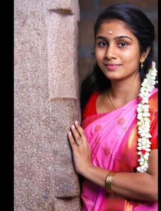 a woman wearing a pink sari standing next to a stone pillar with flowers in her hair