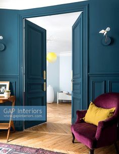 an open door leading into a living room with blue walls and wooden floors in the center