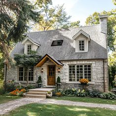 This charming cottage features a classic stone exterior, steep roof with dormer windows, and a welcoming wooden front door. Surrounded by a lush, landscaped garden with blooming flowers and greenery, the large windows brighten the interior. A stone pathway leads to the entrance, enhancing the cottage's quaint and inviting atmosphere, making it the perfect Pinterest-worthy retreat. Single Story Houses Exterior, Country House Small Cottage Style, Cottage With French Doors, Tutor Homes Exterior English Cottages, Stone House Windows, Cute House Entrance, Large Cottage Style Homes, Front Gable House, Cottage Brick House