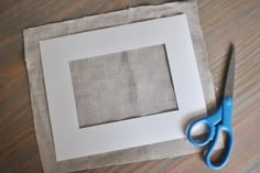 a pair of blue scissors sitting on top of a piece of paper next to a square