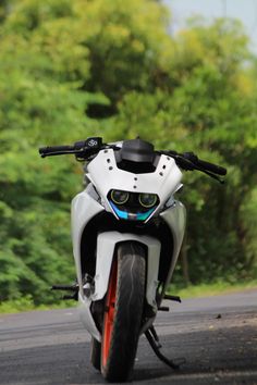 a white motorcycle is parked on the side of the road near some trees and bushes