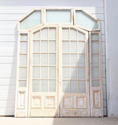 an old wooden door with glass panes on the front and side, against a white wall