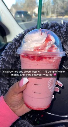 a person holding up a pink drink with whipped cream and strawberries in the cup