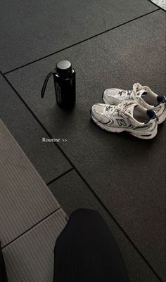 a pair of white sneakers sitting next to a black coffee mug on the ground near a person's feet