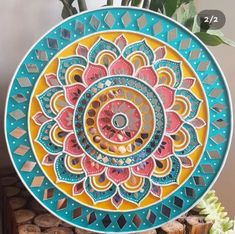 a colorful plate sitting on top of a table next to a potted plant and wooden slices