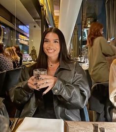 a woman sitting at a table with a glass in her hand and smiling for the camera