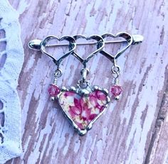 This lovely sterling silver triple-heart brooch with rings was made from pink chintz broken china and recycled into a heart charm that dangles from the brooch. The china charm was decorative soldered with a lead free silver solder. The china piece measures 3/4 inches wide and 3/4 inch long. The china charm dangles from a sterling silver twisted jump ring at the top of the china piece, There are also pink Swarovski crystals and sterling silver bead caps that are suspended from a sterling silver h Silver Heart Brooches For Gift, Pink Heart-shaped Jewelry For Gift Making, Floral Chintz, Soldered Jewelry, Triple Heart, Broken China Jewelry, Soldering Jewelry, Jewelry Heart, Pink Swarovski