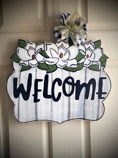 a welcome sign hanging on the front door with flowers and leaves painted on it's side