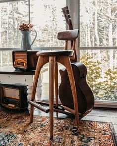 a wooden chair sitting on top of a rug in front of a window next to a guitar