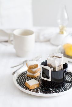 a plate topped with slices of cake next to a cup filled with sugar and tea