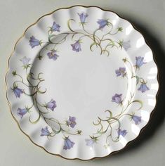 a white plate with purple flowers on the side and gold trimmings around it