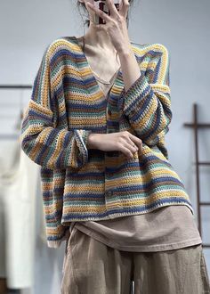 a woman is talking on her cell phone while wearing a multicolored knitted sweater