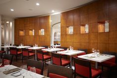 an empty restaurant with red chairs and white tablecloths on the tables in front of wood paneled walls