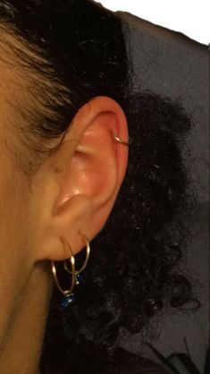 a close up of a person's ear wearing gold hoop earrings and black hair