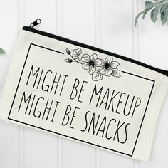 a makeup bag with the words might be makeup might be snacks on it next to a potted plant