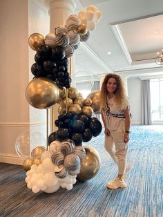 a woman standing in front of a balloon arch with black, gold and white balloons