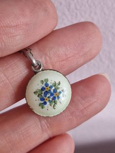 a hand holding a small white and blue flowered pendant