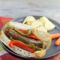 a hot dog with peppers and onions on a plate next to some potato wedges