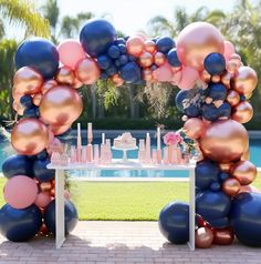 an arch made out of balloons and pink, blue, and gold balloons in front of a pool