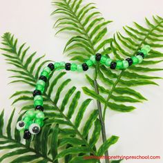 a green and black beaded necklace sitting on top of a fern leaf next to a white wall