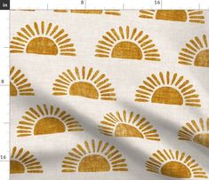 a white and gold sun print fabric with yellow spots on the top, in front of a ruler