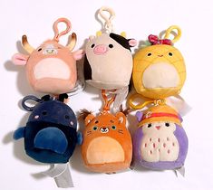 several stuffed animal keychains are lined up on a white surface, one has a clip in it's mouth