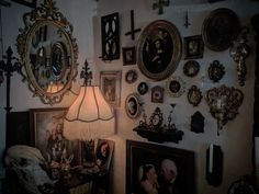 a room filled with lots of framed pictures and wall hangings on the wall next to a lamp