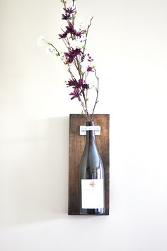 a vase with flowers in it and a wine bottle on a wall mounted shelf next to the wall