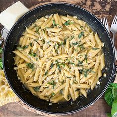 a skillet filled with pasta and spinach on top of a wooden table