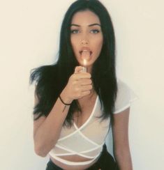 a woman holding a lit candle in her mouth and making a funny face while standing against a white wall