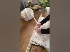 someone is crocheting a blanket on top of a wooden table with flowers in the background