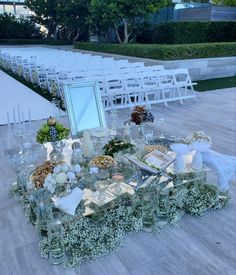 an outdoor wedding setup with white chairs and greenery on the table, surrounded by candles