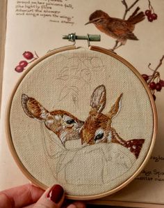 a hand is holding an embroidery hoop with two deers on it