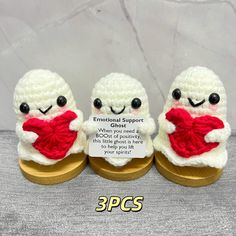 three small crocheted sheeps with red heart on wooden stand, one holding a plaque