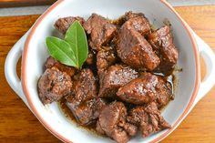 a close up of a bowl of food with meat and a green leaf on top