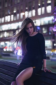 a woman sitting on top of a wooden bench in front of a building at night