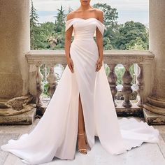 a woman standing in front of a window wearing a white dress with thigh high slits