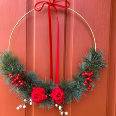 a christmas wreath with red roses and pine needles hanging on a door handle, decorated with holly