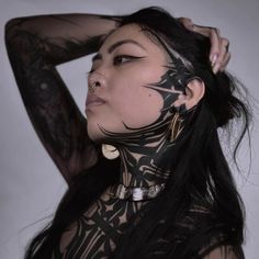 a woman with black tattoos on her body and neck is posing for the camera while holding her hands behind her head