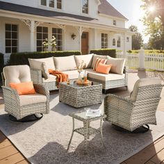 an outdoor living room with wicker furniture and orange pillows on the rugs in front of a white house