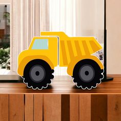 a yellow toy truck sitting on top of a wooden table next to a laptop computer