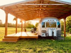 an rv is parked under a covered area in the grass with chairs and tables around it