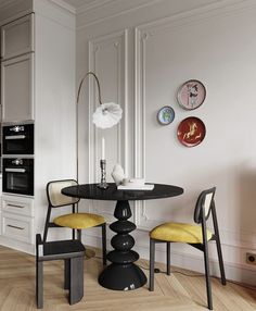 a black table with yellow chairs and plates on the wall in a white walled dining room