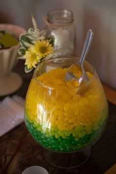 a glass bowl filled with yellow and green candy sits on a table next to other dishes